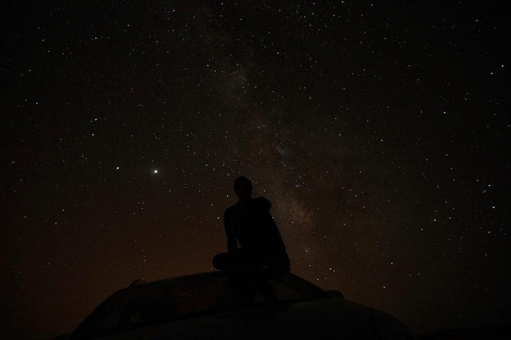 Silhouette of person sitting on car roof under starry night sky, All Angles Creatures theme
