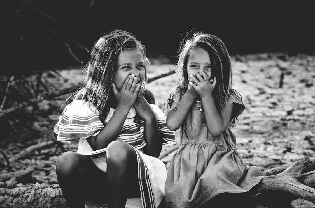 Two young girls laughing outdoors, sitting on a log, black and white photo