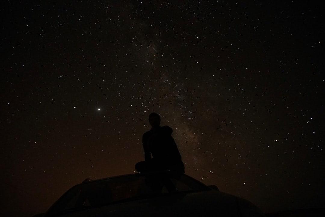 Silhouette of a person stargazing from a car roof under a starry night sky, symbolizing exploration and discovery, relevant to uncovering benefits.