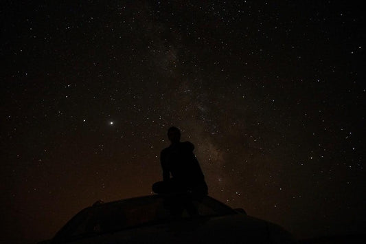 Silhouette of a person stargazing from a car roof under a starry night sky, symbolizing exploration and discovery, relevant to uncovering benefits.