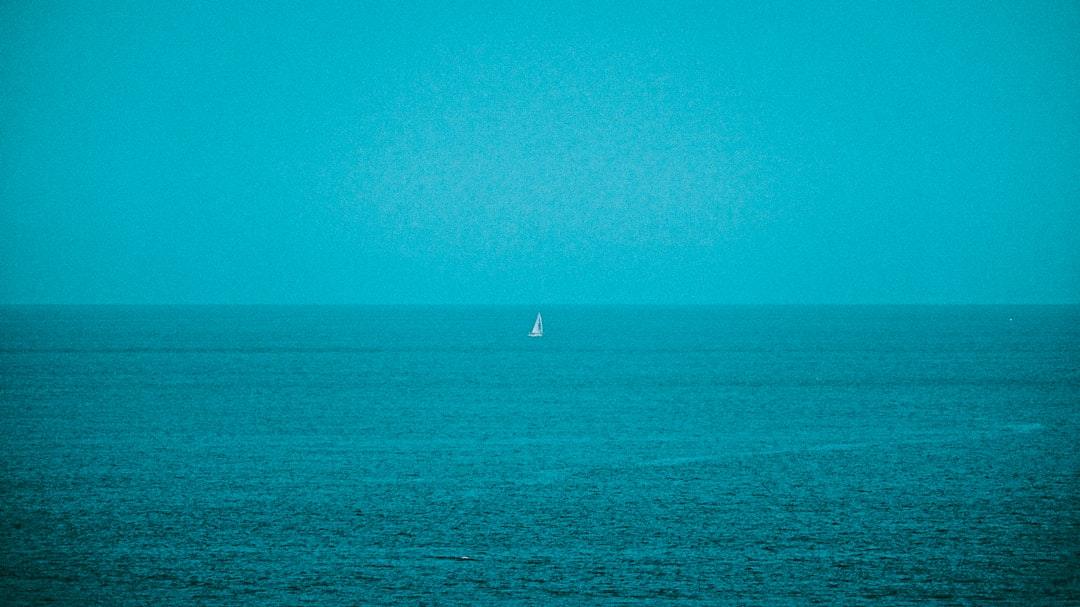 Minimalist ocean scene with a lone sailboat on blue water, calm sea horizon view