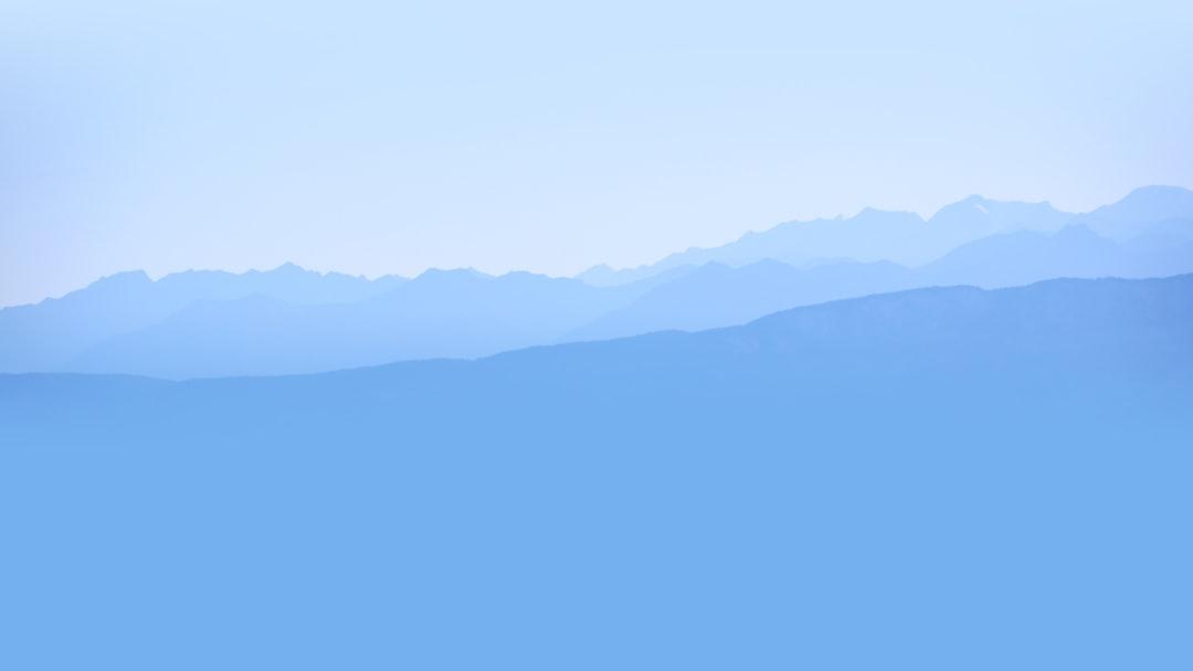 Blue gradient mountain silhouette landscape under clear sky, All Angles Creatures theme.